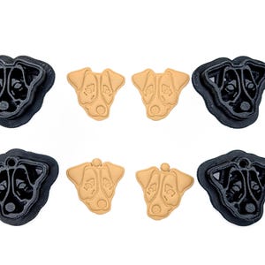 May include: A collection of dog-shaped cookie cutters and cookies. The cutters are black, and the cookies are tan. The dog face design is visible on both the cutters and the cookies. The cutters are made of plastic.