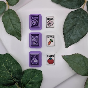 May include: A collection of purple seed packet cutters and seed packet designs. The cutters have the number "20932" and a flower, carrot, and tomato design. The seed packets have the word "SEEDS" and a flower, carrot, and tomato design.