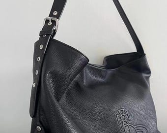 May include: Black leather shoulder bag with a textured finish. The bag features a long strap with a buckle and a debossed emblem on the front. The bag is held by a person.