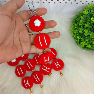 Può includere: Un portachiavi rosso all'uncinetto con dettagli bianchi e la lettera "H" su diversi cerchi rossi. Il portachiavi ha un fermaglio argentato e perline dorate. Il design è fatto a mano e presenta un tocco unico e personalizzato.