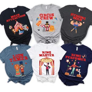 May include: Six graphic t-shirts with circus-themed designs. The shirts are in various colors, including black, gray, white, and blue. Each shirt features a different design, such as "Main Attraction," "Circus Crew," and "Ring Master."