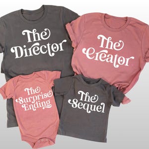 May include: A collection of family matching t-shirts and a baby onesie in grey and dusky pink. Each garment features white text: "The Director", "The Creator", "The Surprise Ending", and "The Sequel".
