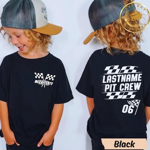 Op de afbeelding: Zwart T-shirt met korte mouwen met een racethema. De voorkant heeft een geblokt vlagontwerp en de naam "McCAFFERTY". De achterkant toont "LASTNAME PIT CREW" en het nummer "06" met een geblokte vlag. Het woord "Black" staat onderaan.