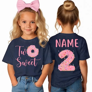 May include: Two young girls wearing navy blue t-shirts with pink text and donut graphics. The front of the shirt says "Two Sweet" with a donut. The back of the shirt says "Name" and a number 2 shaped like a donut.