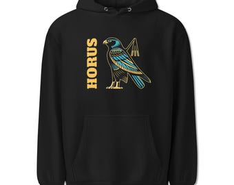 May include: A black hooded sweatshirt featuring a graphic of a falcon in profile, colored in shades of blue and gold. The text HORUS is printed vertically in gold capital letters to the left of the bird, which holds a flail symbol.