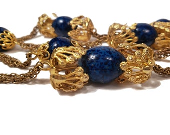 Puede incluir: Un collar de cadena dorada con cuentas azules y doradas. Las cuentas son redondas y tienen una superficie texturizada. La cadena está hecha de pequeños anillos unidos.