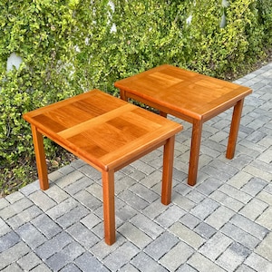 May include: Two wooden side tables in a warm, reddish-brown hue. Each table features a square top with a cross design and four straight legs. The tables measure approximately 61 cm long, 61 cm wide, and 51 cm high.
