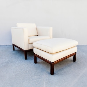 May include: Cream-colored armchair and matching ottoman set. The furniture features a minimalist design with dark brown wooden frames and legs. The cushions and upholstery are a light cream color, creating a clean and modern aesthetic.