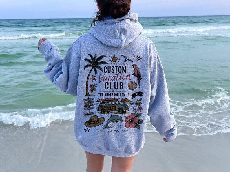 May include: A light gray hooded sweatshirt featuring a back graphic with the text CUSTOM VACATION CLUB THE ANDERSON FAMILY EST. 2026. The design includes a palm tree, a parrot, a station wagon with a surfboard, a dolphin, a sun, and flowers.