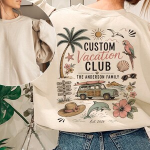 May include: A beige crewneck sweatshirt featuring a graphic on the back with a palm tree, a parrot, a surfboard on a station wagon, a sun, a dolphin, a straw hat, and flowers. The text reads CUSTOM Vacation CLUB, THE ANDERSON FAMILY, and Est. 2026.