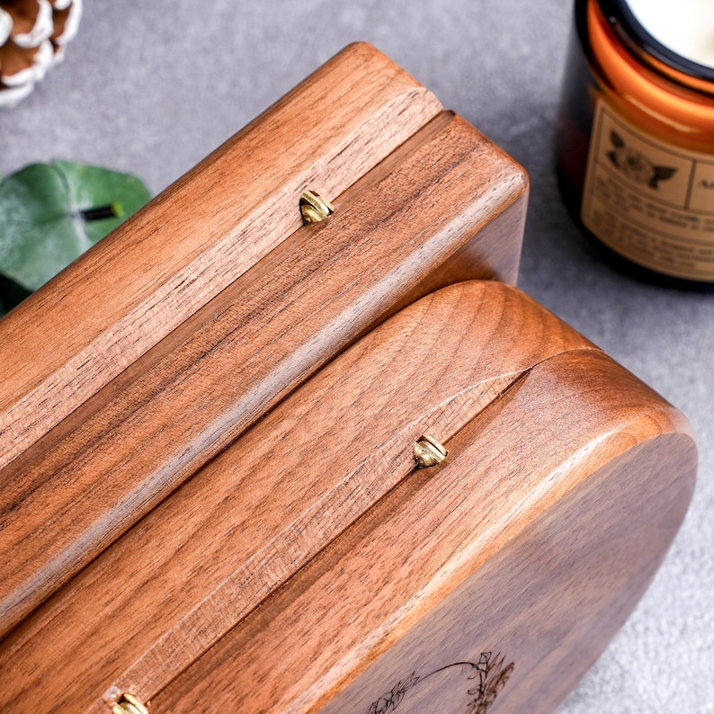May include: Close-up of two wooden boxes with a warm brown finish. The boxes have rounded edges and are secured with small, gold-colored metal clasps. The wood grain is visible, and the boxes appear to be handcrafted.