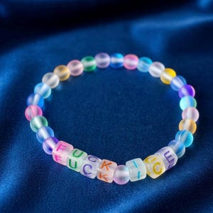 May include: A circular bracelet composed of translucent, frosted, multi-colored beads. Several square beads are interspersed, featuring the printed text FUCK ICE in vibrant, multi-colored lettering. The beads display a gradient of colors.
