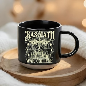 May include: Black ceramic mug with the text "BASGIATH WAR COLLEGE" in a gothic font. The mug features a detailed illustration of a winged creature, a castle, and celestial elements. The mug sits on a wooden tray.