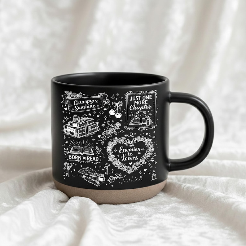 May include: Black ceramic mug with a tan base, featuring white illustrations and text. The design includes phrases like "Grumpy x Sunshine," "Just One More Chapter," and "Enemies to Lovers," along with book and floral motifs. The mug has a curved handle.