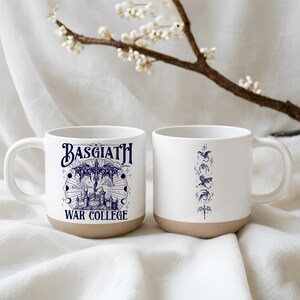 May include: Two white ceramic mugs with a tan base. One mug features the text "BASGIATH WAR COLLEGE" in navy blue, with a castle and celestial design. The other mug has a navy blue dragon design.