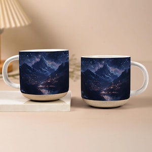 May include: Two ceramic mugs with a mountain landscape design. The mugs feature a night sky with stars, snow-capped mountains, and a town at the base of the mountains. The mugs have a white handle and a beige base.