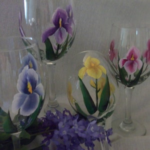 May include: Four clear glass wine glasses with hand-painted iris flowers. The glasses feature purple, yellow, and pink irises with green leaves.
