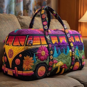 Pode incluir: Uma colorida mala de viagem acolchoada com um design vibrante de uma carrinha VW vintage com detalhes florais e paisagísticos. A mala tem uma base preta com detalhes em amarelo, laranja, rosa e roxo, e alças decoradas com flores.
