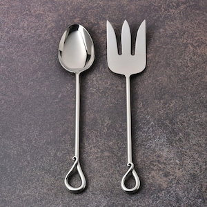 May include: A stainless steel serving spoon and fork set. The spoon has an oval bowl, and the fork has three tines. Both utensils have long, slender handles with a teardrop-shaped design at the end.