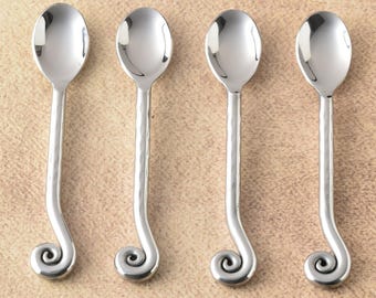 May include: Four silver spoons with oval bowls and hammered, curved handles ending in a decorative spiral. The spoons are arranged on a light brown surface, reflecting light.