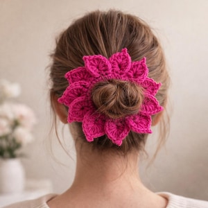 Puede incluir: Un vibrante accesorio para el cabello de ganchillo fucsia, con forma de flor, se usa en un moño. La pieza de cabello hecha a mano agrega un toque de color y textura. El accesorio para el cabello es una adición elegante a cualquier peinado.