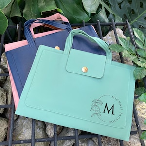 May include: Three leather tote bags in shades of teal, navy, and pink. The teal bag features a flap with a gold button and a circular design with the letter "M" and the name "Michael Jackson".
