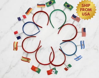 May include: A collection of headbands with flags of various countries, including the USA, Brazil, and Germany. Each headband features a spring and a small flag. The text "Get Ready for World CUP 2026" is at the top.