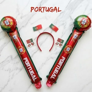 Puede incluir: Dos bastones de animaci&oacute;n inflables rojos y verdes con la bandera de Portugal y el texto PORTUGAL, una diadema roja con dos peque&ntilde;as antenas de bandera, y dos pegatinas cuadradas con la bandera de Portugal y un coraz&oacute;n rojo.