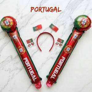 May include: Two inflatable red and green cheering sticks featuring the Portugal flag and the word PORTUGAL, a red headband with two small Portugal flag antennae, and two square stickers displaying the Portugal flag and a red heart shape.