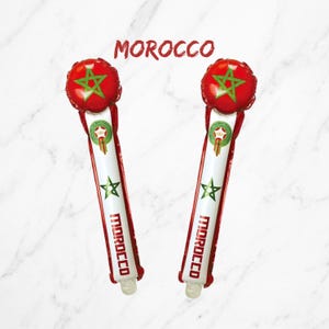 Puede incluir: Dos bastones de animaci&oacute;n inflables con los colores rojo y verde de la bandera de Marruecos. Cada bast&oacute;n tiene una parte superior circular con una estrella verde, una secci&oacute;n central blanca con el texto MOROCCO y un peque&ntilde;o emblema.