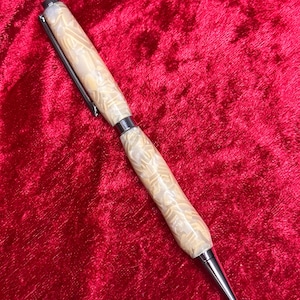 May include: A handcrafted pen with a cream-colored, patterned barrel and silver accents. The pen features a silver clip and a pointed tip. The pen is displayed against a red velvet background.