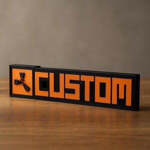May include: A black and orange rectangular sign with the word "CUSTOM" in orange block letters. The sign has a unique design element on the left side. The sign is displayed on a wooden surface.
