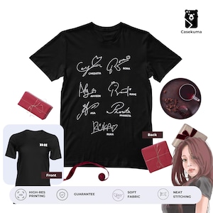 May include: Black t-shirt featuring white signatures of several people. The signatures are arranged in a grid pattern. The shirt also has a small logo on the front. The image includes a gift box and a cup of tea.