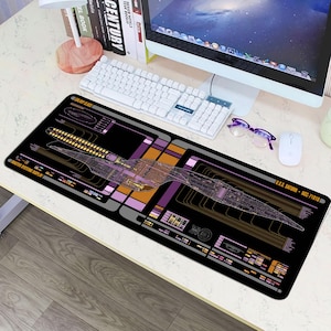 May include: Black rectangular mousepad featuring a schematic design of a starship, with orange, purple, and gray accents. The text "U.S.S. SATURN - NCC-71818" is visible. The mousepad is designed for computer use.