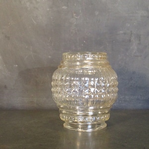 Puede incluir: Una pantalla de lámpara de vidrio transparente con un patrón de diamante texturizado. La pantalla tiene un borde dorado y una forma redondeada.