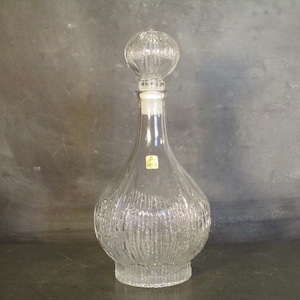 May include: A clear glass decanter with a textured surface and a round, clear glass stopper. The decanter has a wide base and a narrow neck.