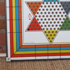 Op de afbeelding: Een vintage spelbord met een stervormig speelgebied. Het bord is gemaakt van metaal en heeft een witte achtergrond met rode, gele, blauwe en groene secties. Het bord is gelabeld "Made in Canada".