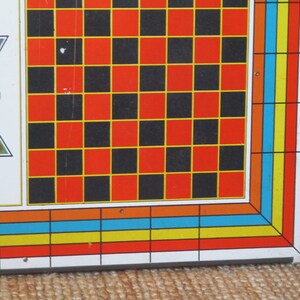 Op de afbeelding: Een vintage spelbord met een schaakbordpatroon in zwarte en rode vierkanten met gele randen. Het bord heeft een kleurrijke rand met oranje, blauwe en gele strepen.
