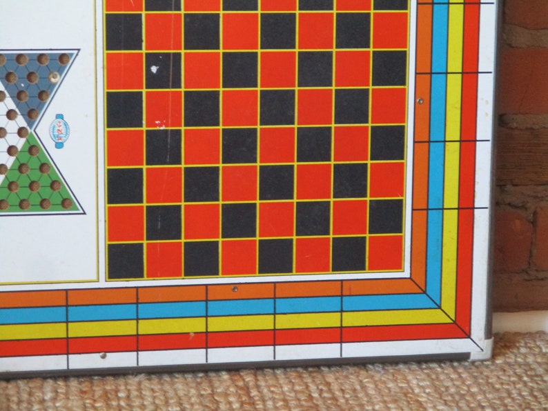 Op de afbeelding: Een vintage spelbord met een schaakbordpatroon in zwarte en rode vierkanten met gele randen. Het bord heeft een kleurrijke rand met oranje, blauwe en gele strepen.
