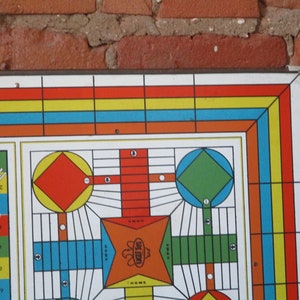 Op de afbeelding: Een vintage spelbord met een kleurrijk ontwerp. Het bord heeft een centrale ster met de woorden "Eagle Tus" en de nummers 1 tot en met 62 rond de rand.