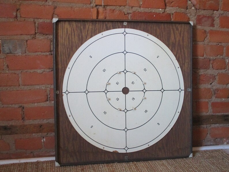 Op de afbeelding: Een vintage houten dartbord met een wit doel en zwarte ringen. Het doel heeft de nummers 5, 10, 15 en 21 erop gedrukt.