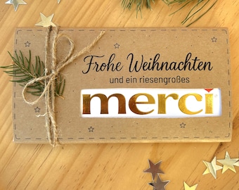 May include: A kraft paper gift box tied with twine, featuring the words "Frohe Weihnachten" and "merci" in gold lettering. The box is decorated with star-shaped confetti and a sprig of pine.