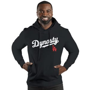 May include: Black hooded sweatshirt with the word "Dynasty" in white script across the chest. A red "LA" logo is below the word. The sweatshirt has a front pocket and a hood.