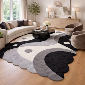 Może przedstawiać: Duży, nowoczesny dywan z wzorem yin-yang w kolorach czarnym, szarym i złamanej bieli. Dywan ma falisty brzeg i leży na drewnianej podłodze w salonie.