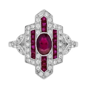 Peut inclure: Bague en argent au design Art Déco. La bague présente un grand rubis ovale au centre, entouré de petits rubis et de pierres précieuses rondes et transparentes. Le design de la bague est symétrique et élégant.