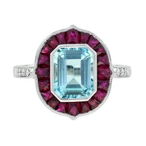 Può includere: Un anello d'argento con una grande gemma rettangolare azzurra al centro, circondata da un alone di gemme rosse scure più piccole. La fascia dell'anello presenta dettagli delicati e piccole pietre di accento.