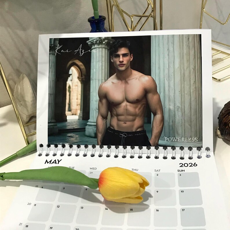 May include: A calendar for the year 2026, open to May, featuring a photograph of a shirtless man. The calendar has a spiral binding and a yellow tulip rests on the calendar page. The word "POWERLESS" is visible.