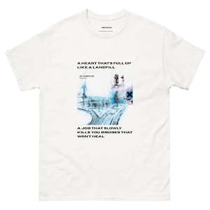 May include: A white short-sleeve t-shirt featuring a graphic print with the text A HEART THAT'S FULL UP LIKE A LANDFILL, OK COMPUTER, RADIOHEAD, and A JOB THAT SLOWLY KILLS YOU, BRUISES THAT WON'T HEAL, along with a blue and white abstract image.