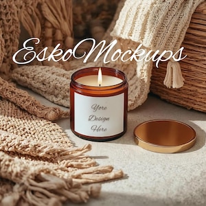 Könnte beinhalten: Eine brennende Kerze in einem braunen Glas mit einem goldenen Deckel. Die Kerze hat ein weißes Etikett mit dem Text "Yore Design Here". Der Hintergrund umfasst einen geflochtenen Korb und eine beige Strickdecke.
