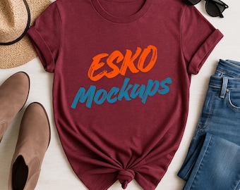 Op de afbeelding: Een bordeauxrood t-shirt met de tekst "ESKO Mockups" in oranje en blauw. Het shirt is gestyled met een strohoed, bruine laarzen, zonnebril en een spijkerbroek. Het shirt is aan de onderkant geknoopt.